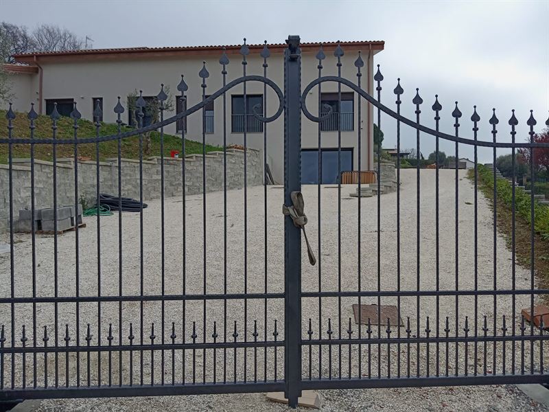 Cancello carraio a due ante in ferro grigio scuro, con lance decorative e volute